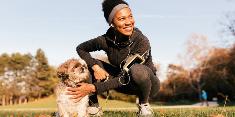 Uma atleta negra pratica atividades físicas feliz em um parque junto com seu cãozinho